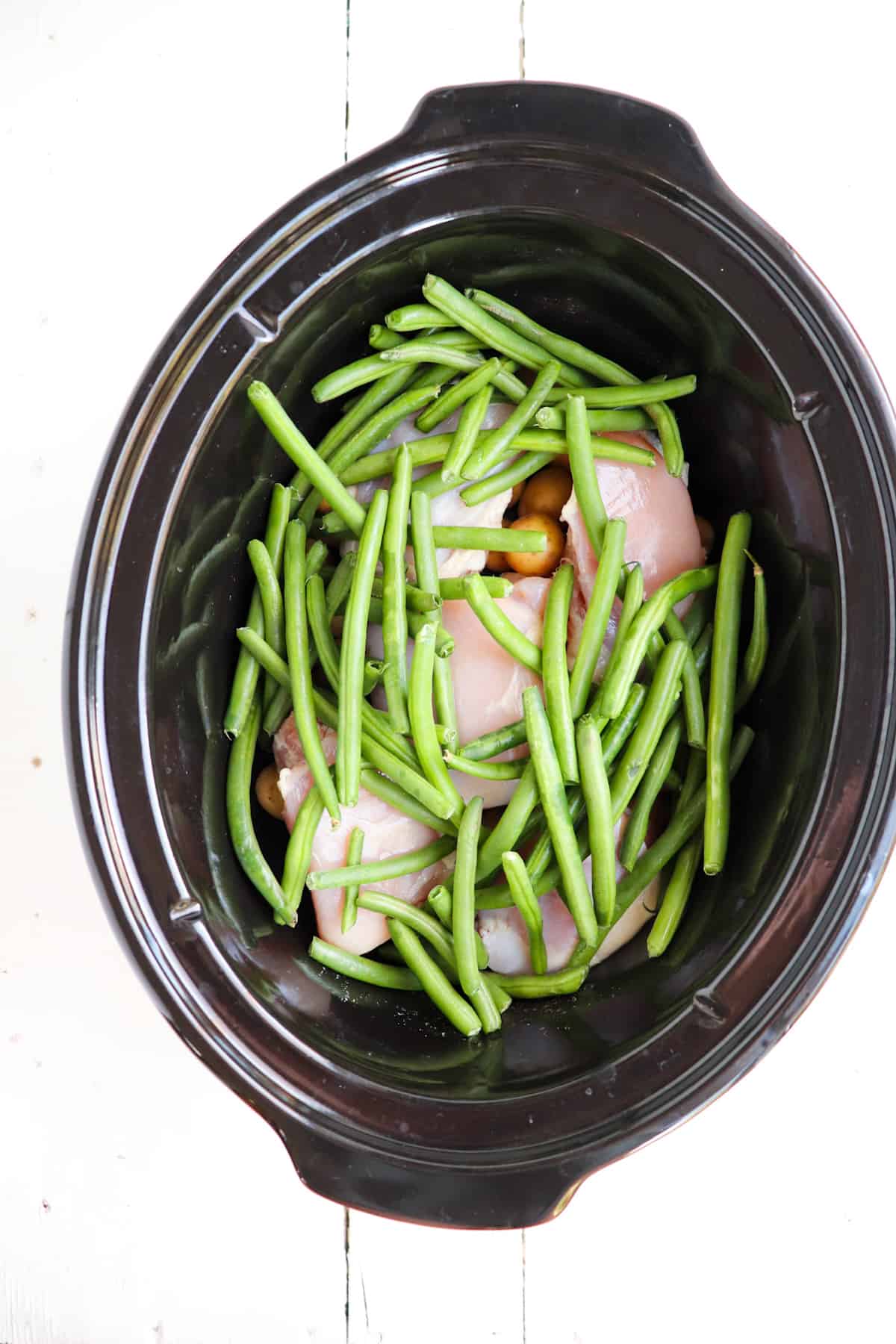 fresh green beans added on top of other ingredients in the crock pot.