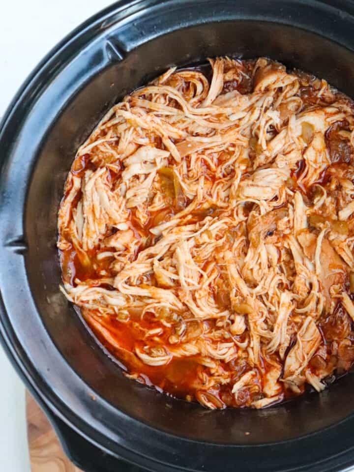 shredded chicken cooking in slow cooker pot.