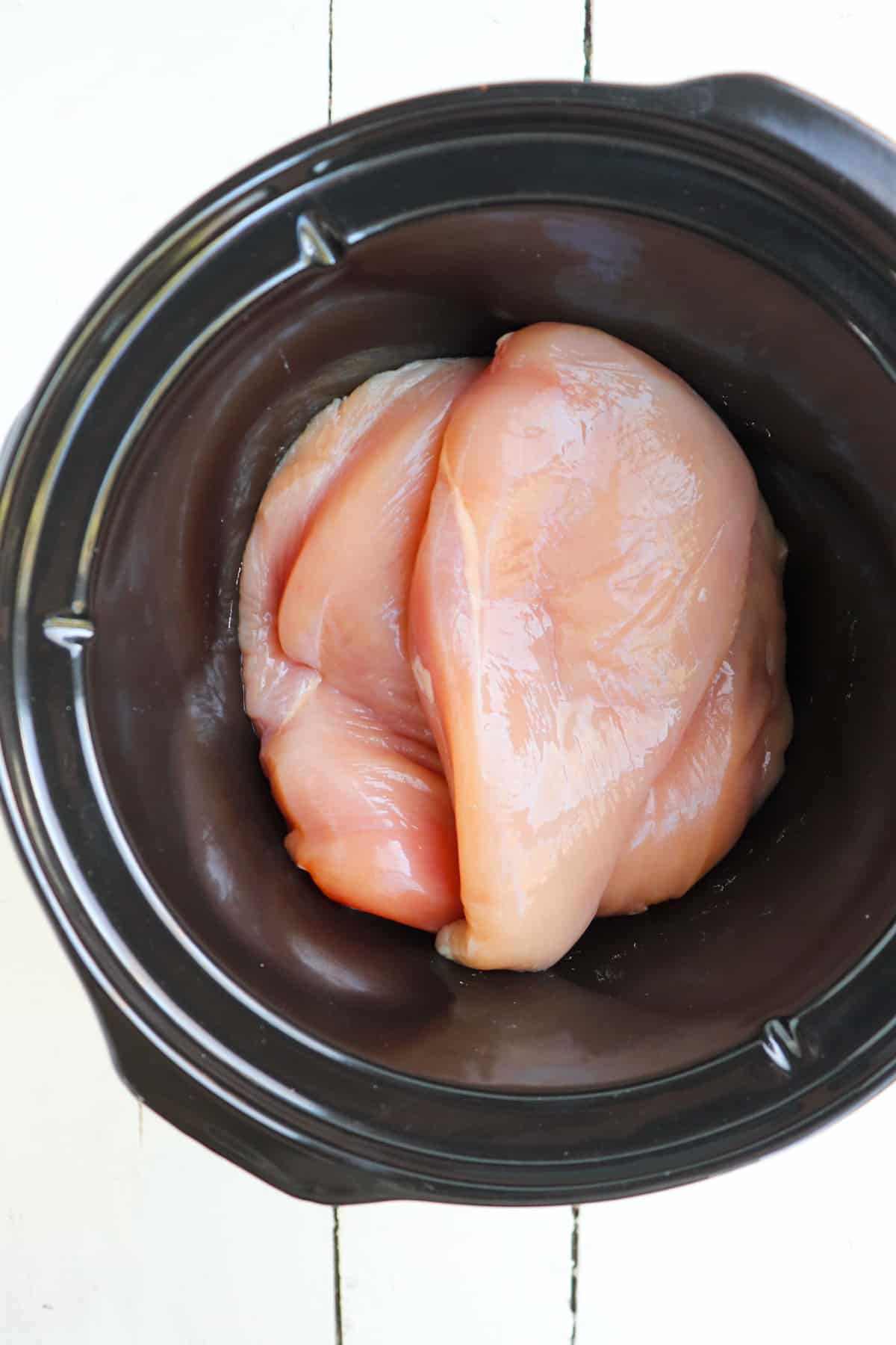 raw chicken breasts in slow cooker pot.