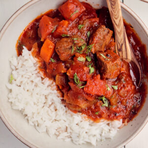 close up of bowl of african stew with rice and a wooden spoon.