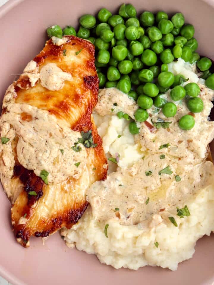 up close of boursin chicken with mashed potatoes and peas covered in sauce.
