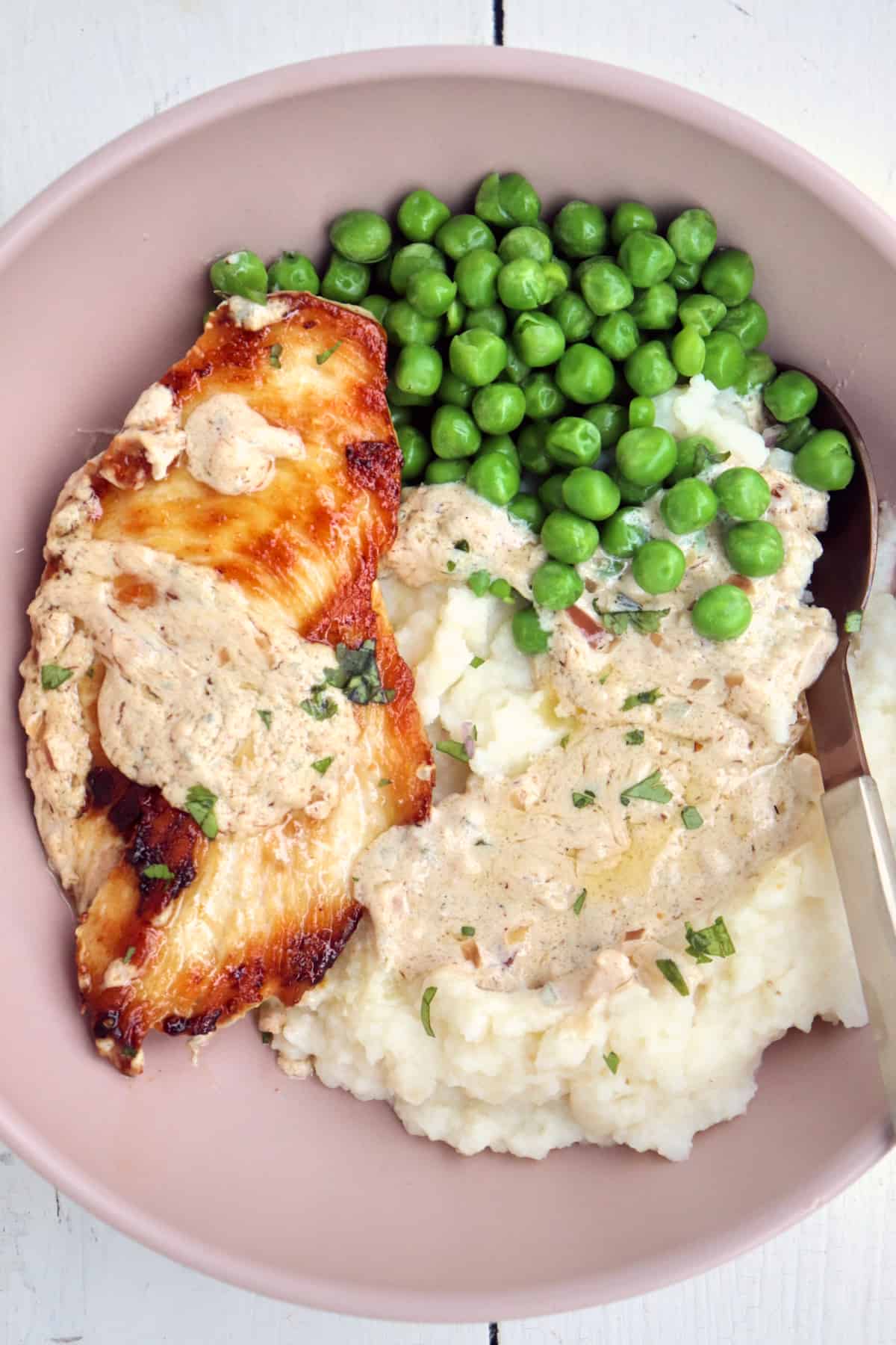 browned chicken with boursin sauce, mashed potatoes, and peas in a pink bowl.
