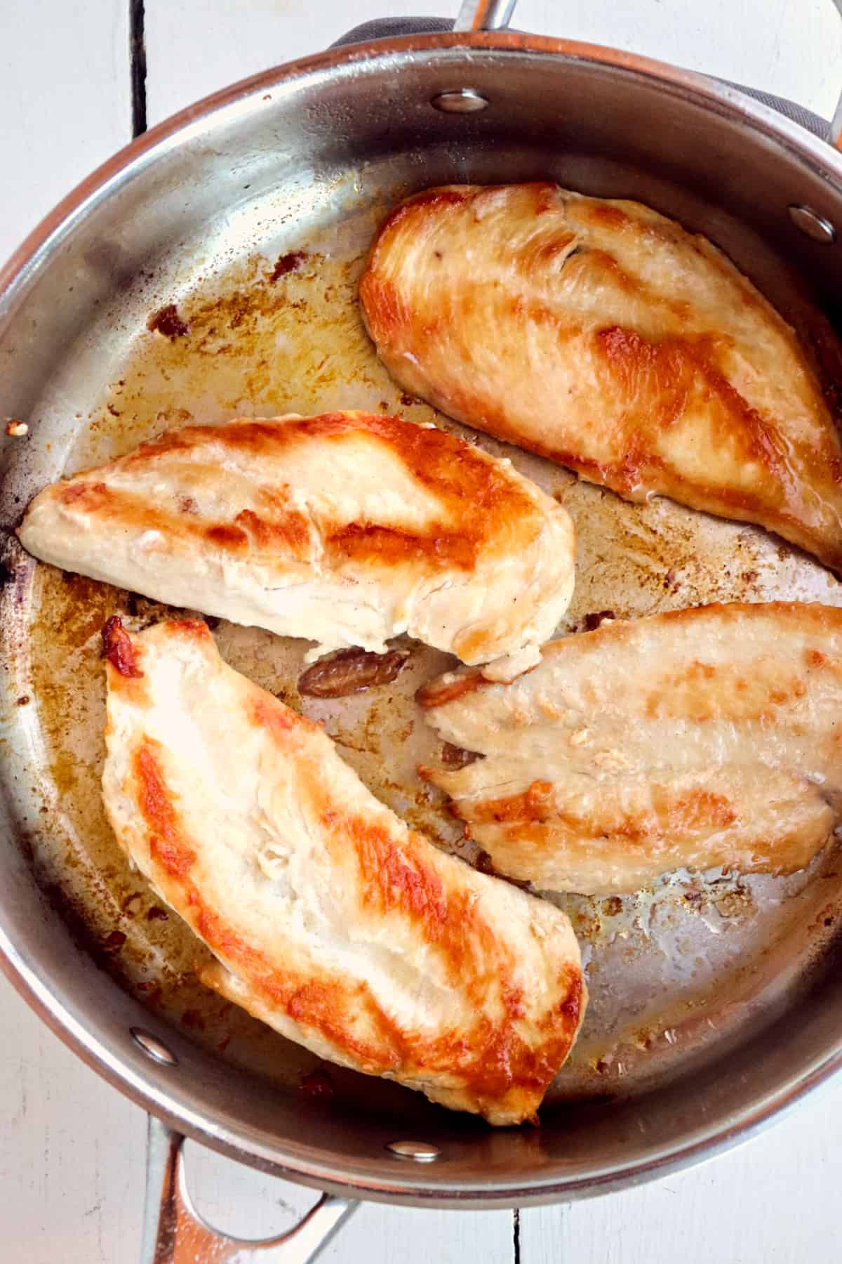 four browned chicken breasts in a skillet.