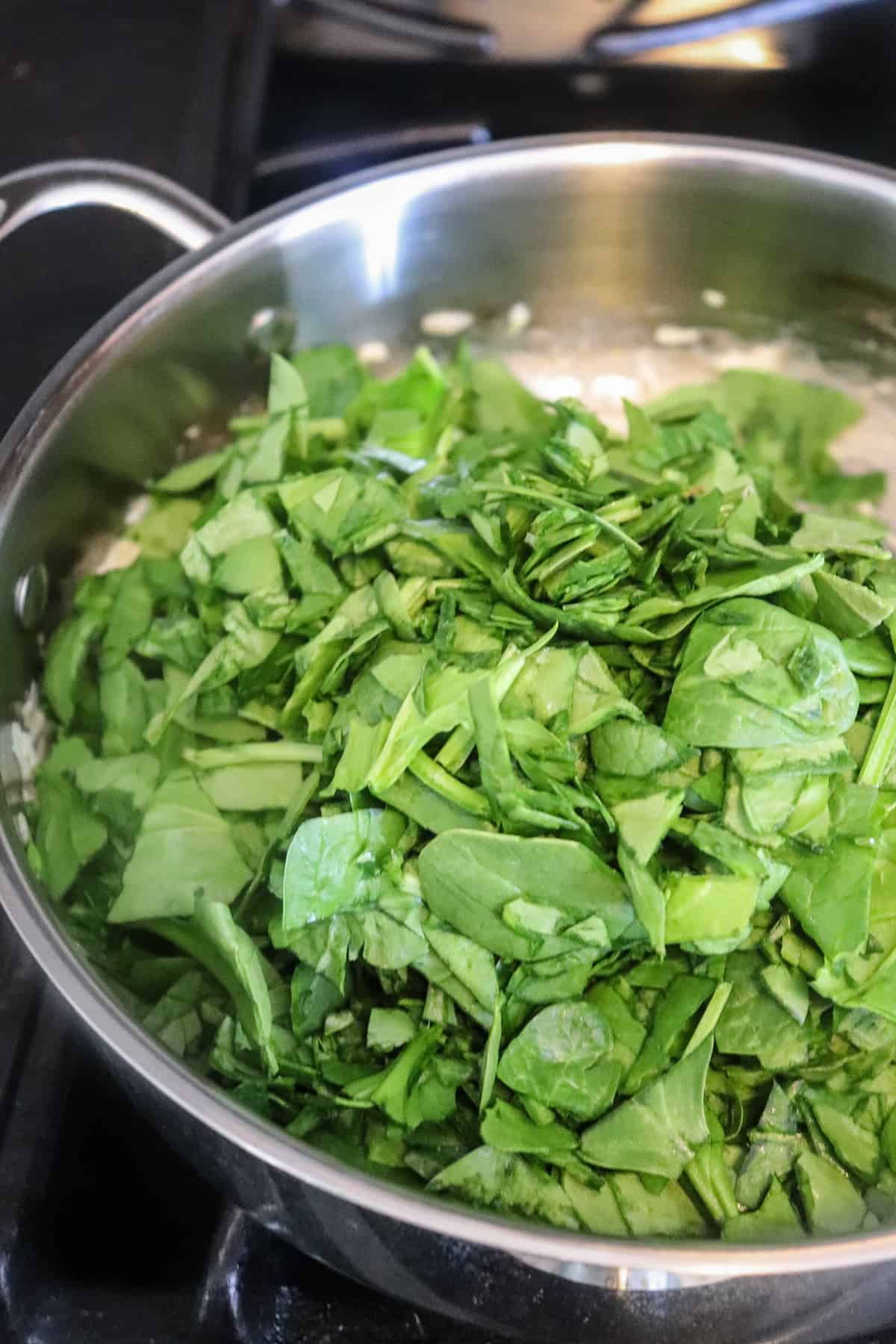 chopped spinach added to a skillet.