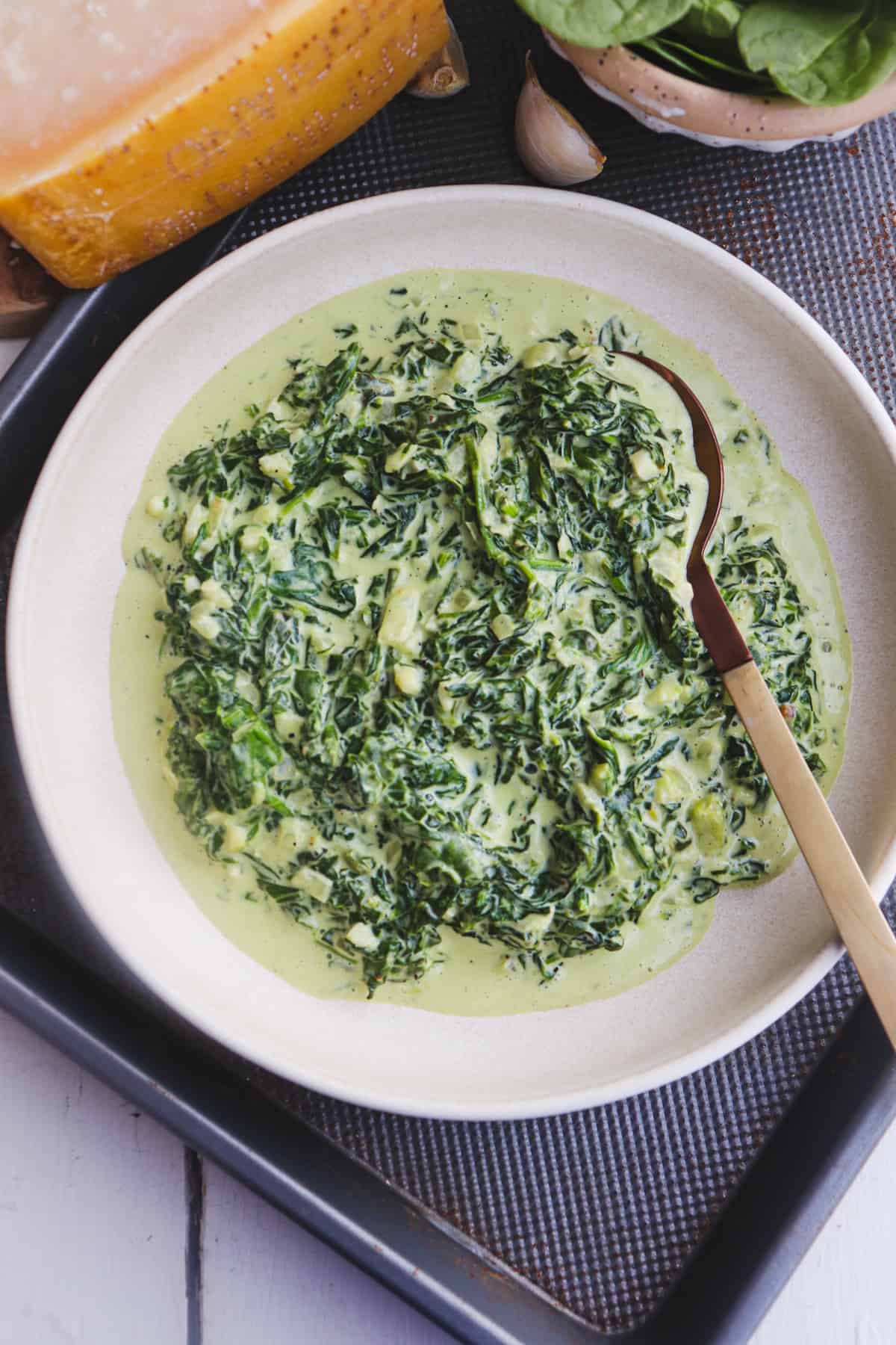 creamed spinach in a bowl with a serving spoon and ingredients in the background.