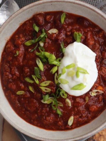 venison chili topped with green onion and sour cream in a grey bowl.