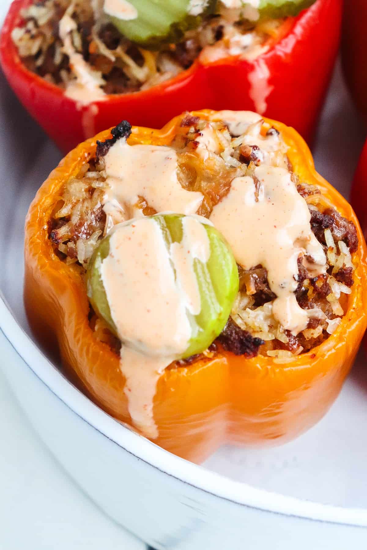 stuffed yellow bell pepper topped with sauce and a pickle.