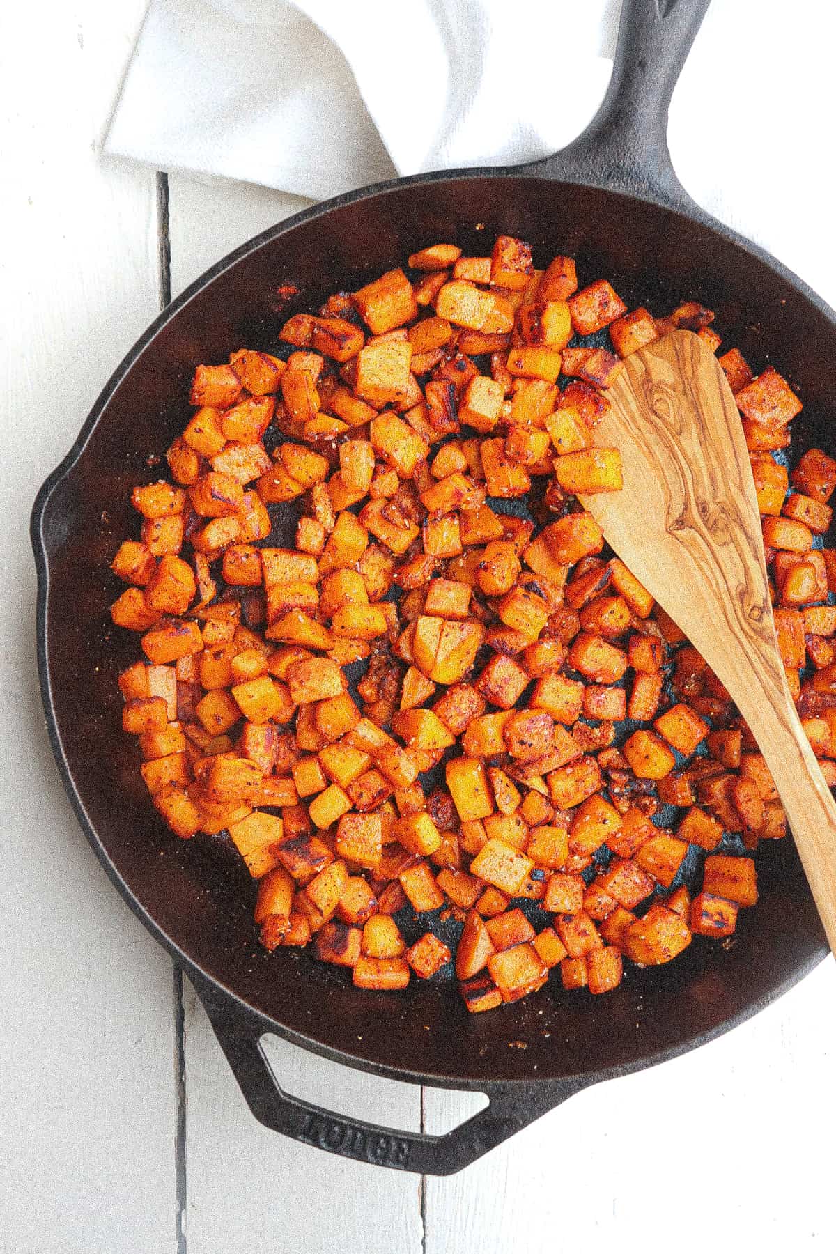 sauteed sweet potatoes in cast iron skillet stirred with a wooden spoon.