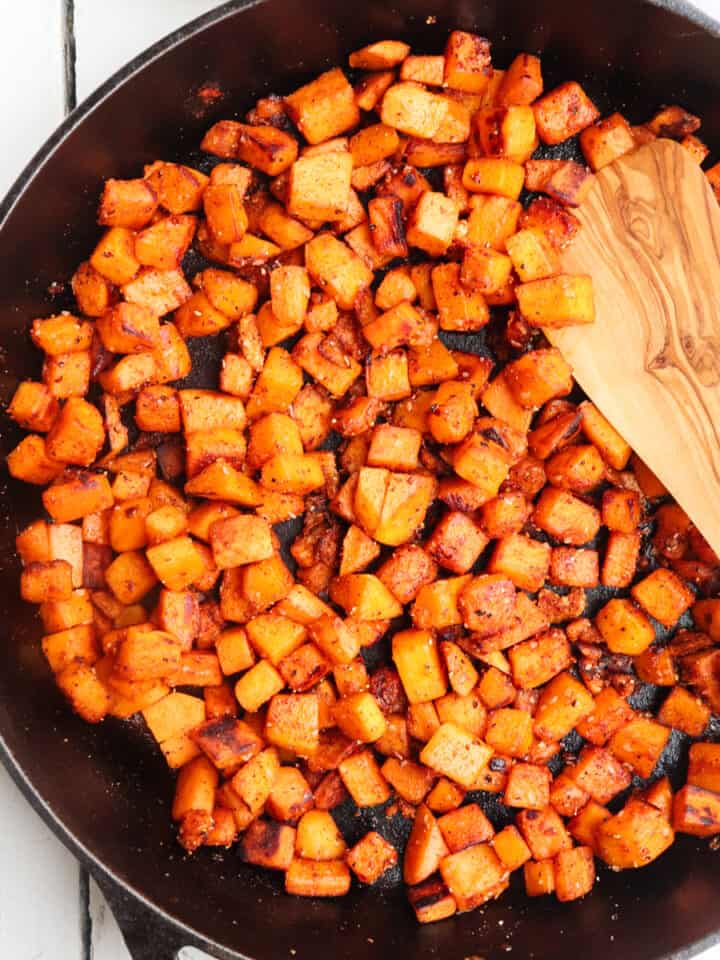 sauteed sweet potatoes in cast iron skillet stirred with a wooden spoon.