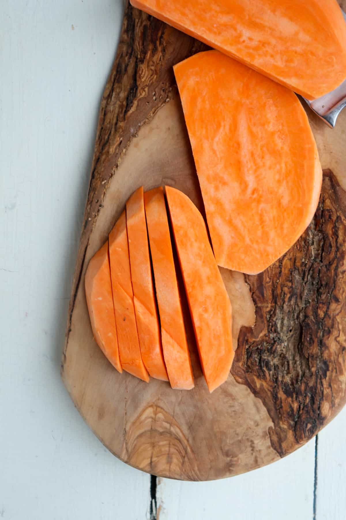 sweet potatoes being sliced into matchsticks on a wooden board.