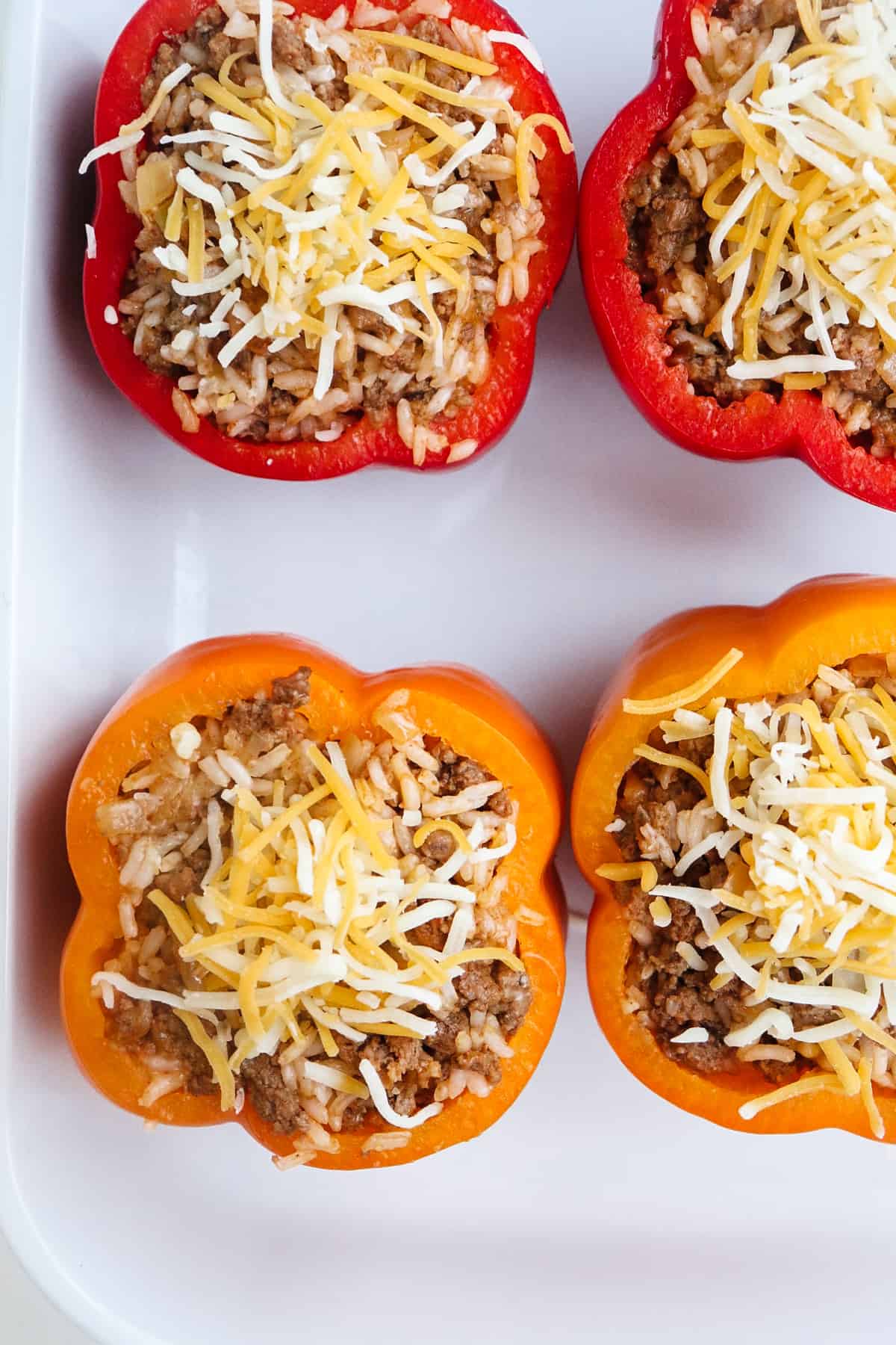 four uncooked stuffed peppers in a white baking dish.