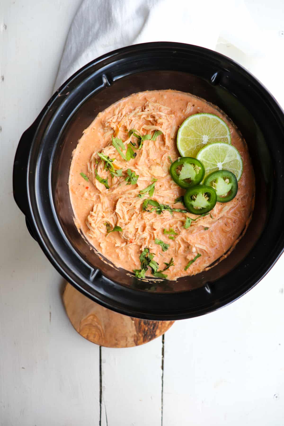 finished slow cooker salsa chicken topped with limes, cilantro, and jalapeno.