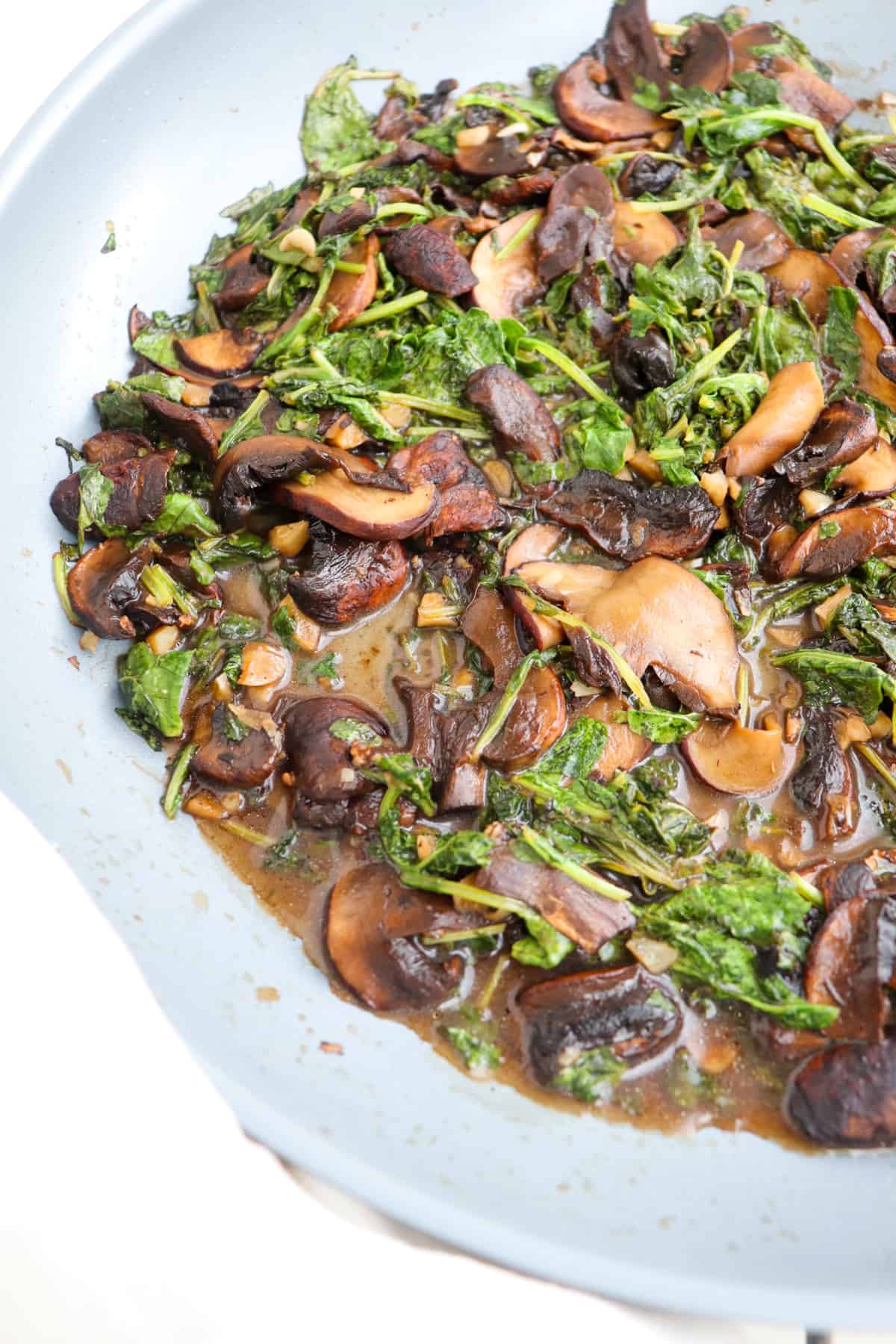 finished sauteed mushrooms and kale with balsamic in a pan up close.