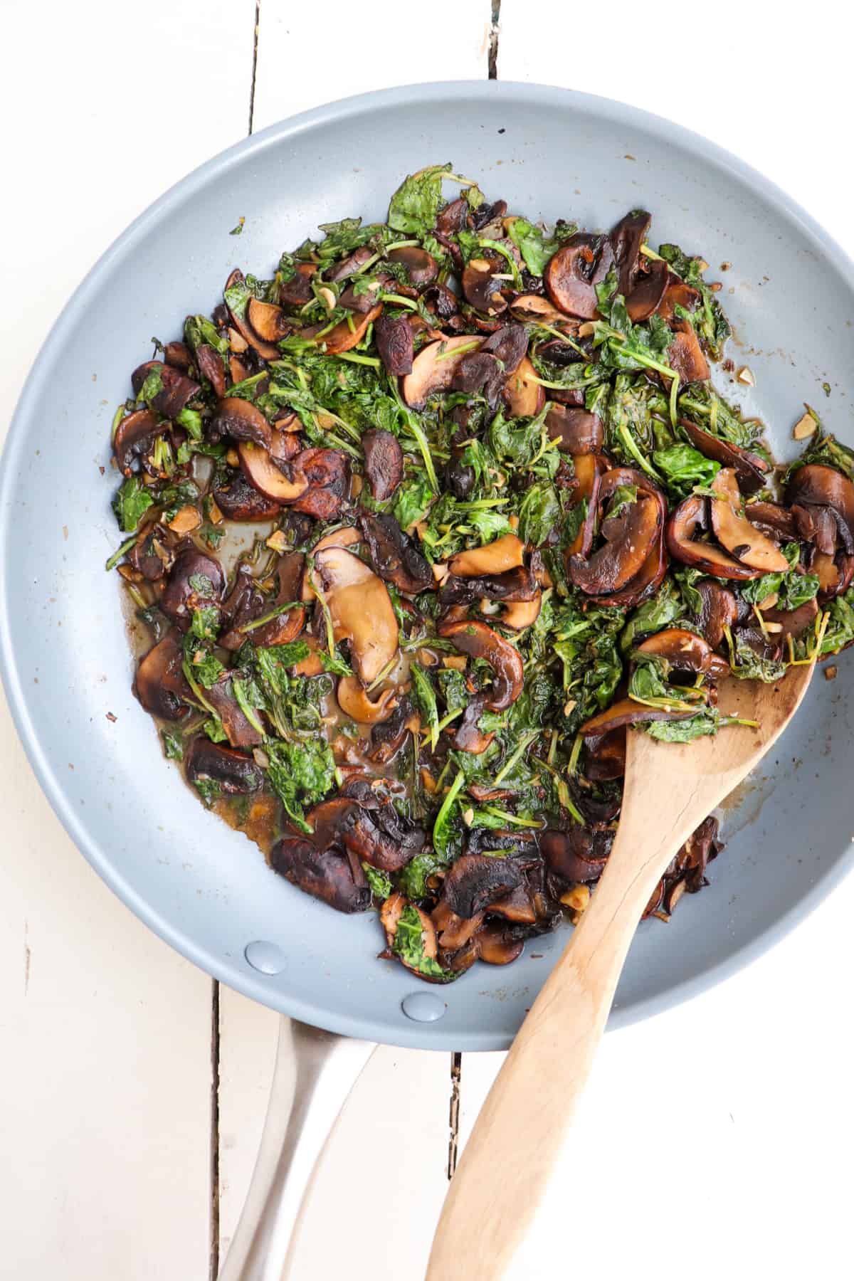 sauteed mushrooms and kale in a pan with a wooden spoon.