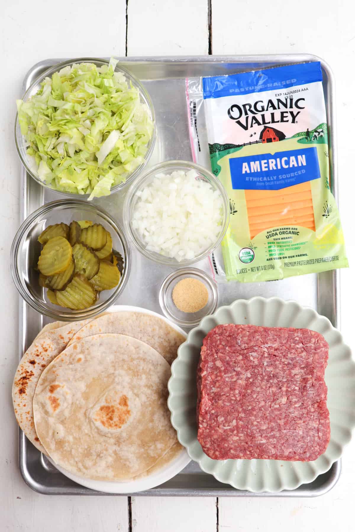 ingredients for smash burger tacos on a metal tray.
