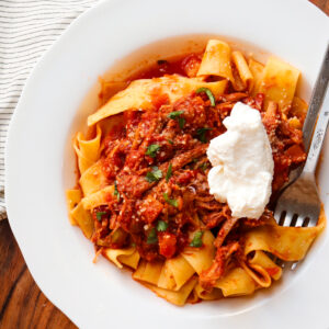 beef ragu that has been topped with ricotta on a white plate.