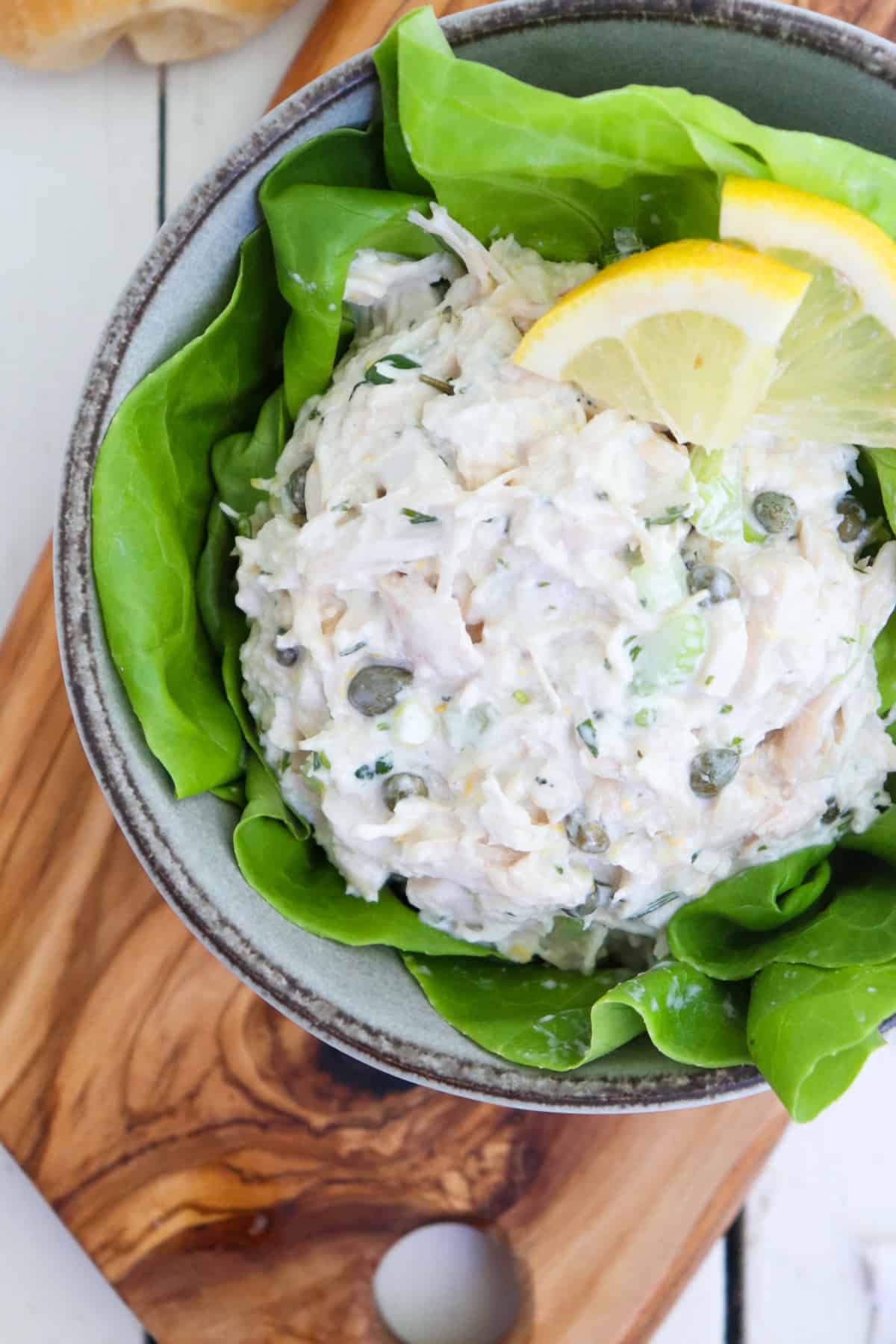 scoop of caper chicken salad on a bed of lettuce with two small lemon wedges.