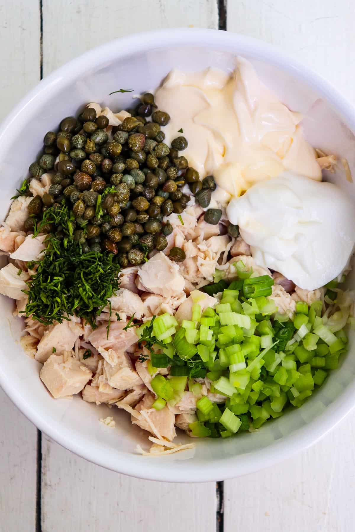 caper chicken salad ingredients unmixed in a white bowl.