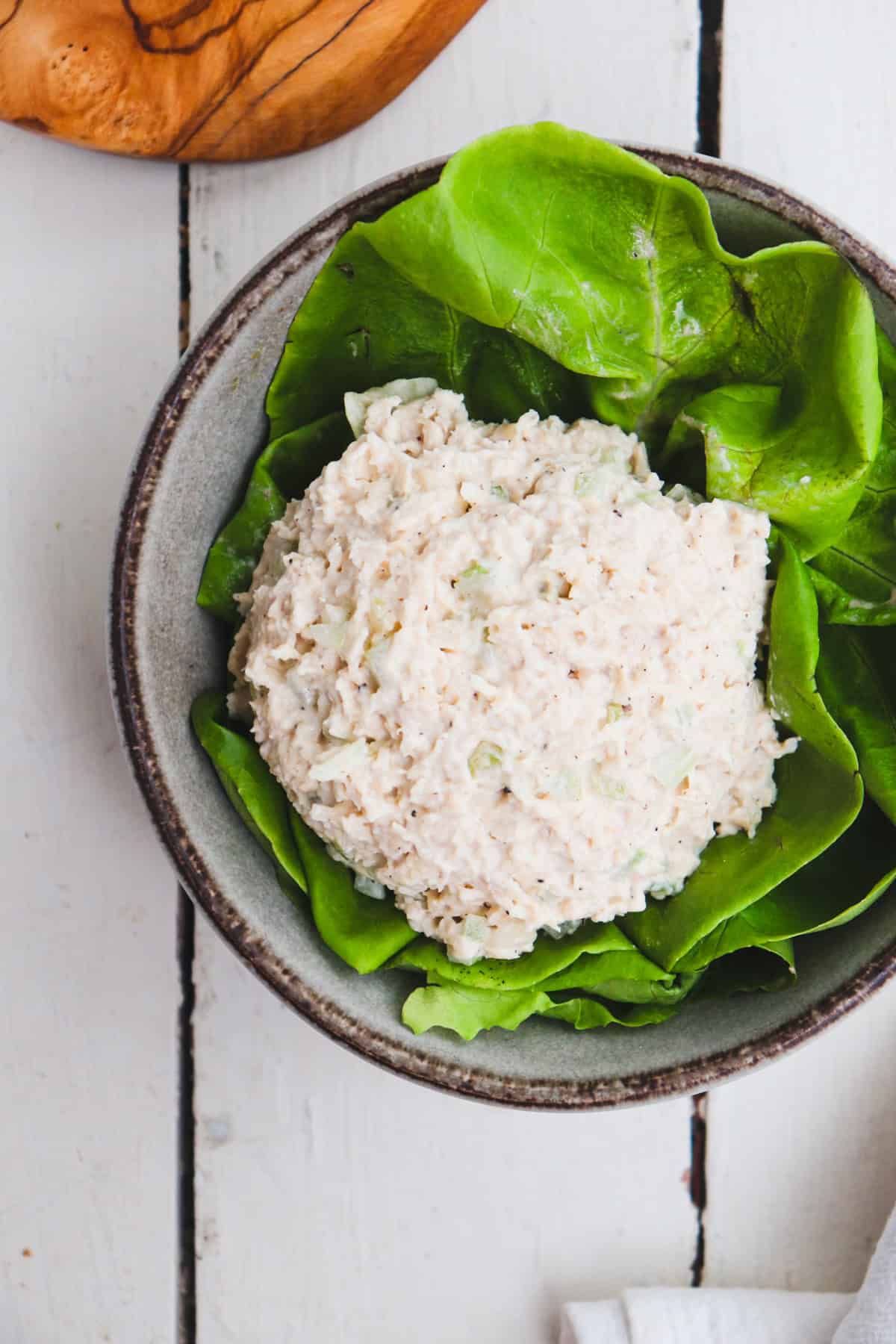scoop of chicken salad in a bowl filled with lettuce with croissants to the side.