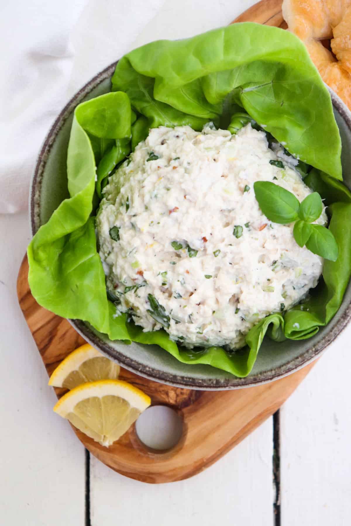 scoop of lemon chicken salad in a bowl of lettuce with lemon and basil for garnish.