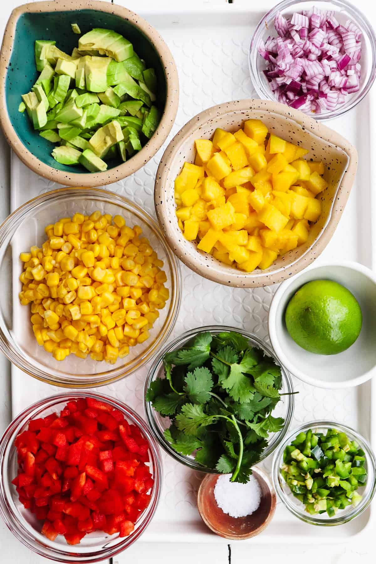 ingredients for mango corn salsa on a white tray.