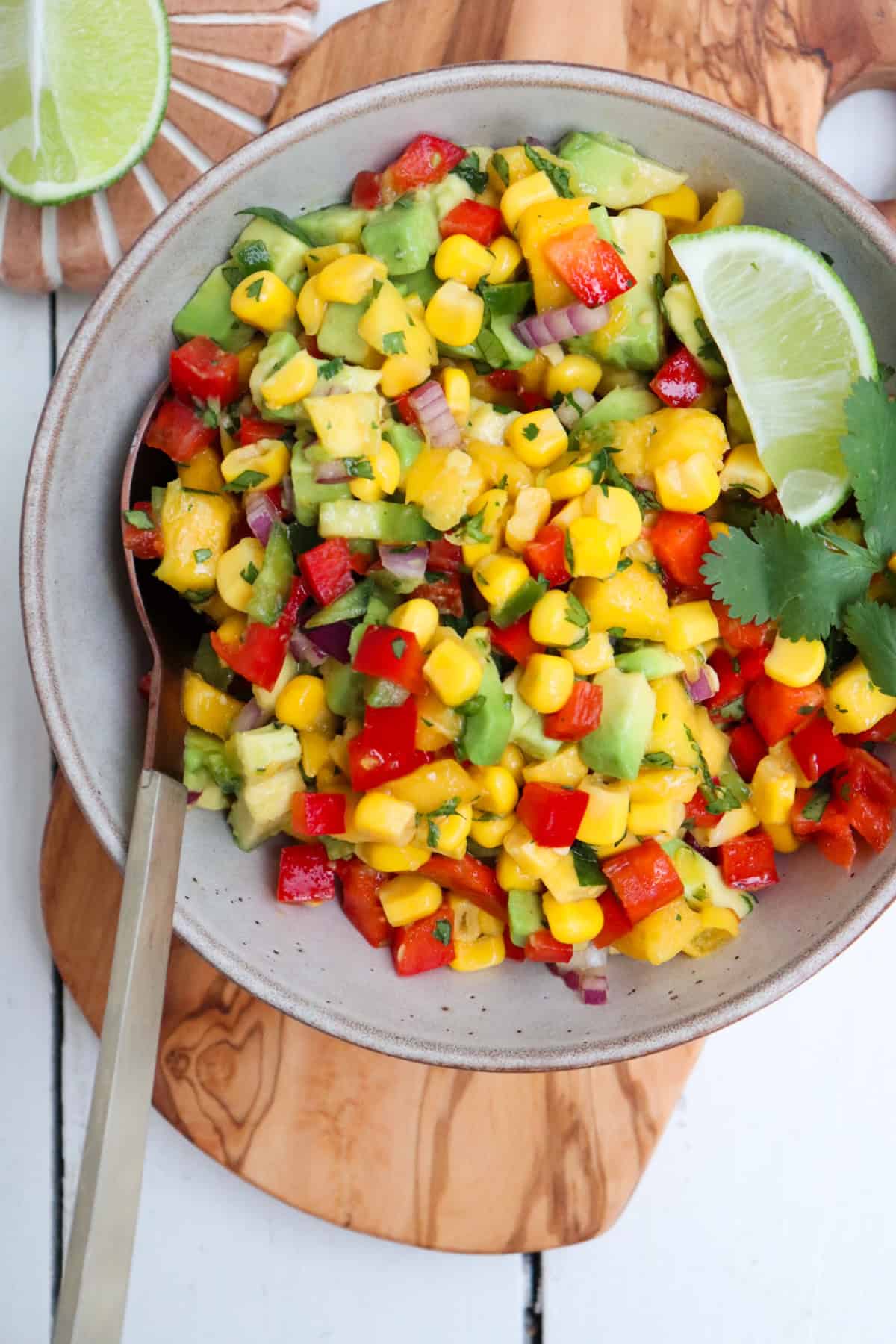 bowl of finished mango corn salsa with a spoon and lime wedges.