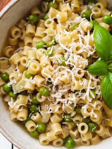 bowl of piselli and pasta garnished with grated parmesan and basil.