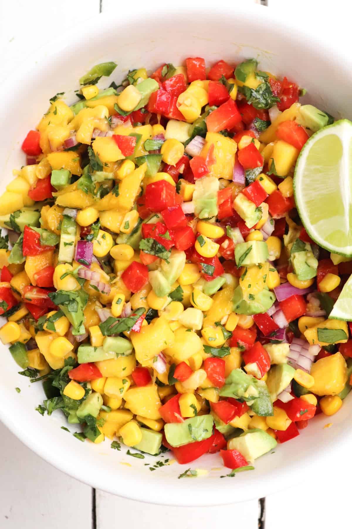 finished mango corn salsa in a white bowl with lime wedges.