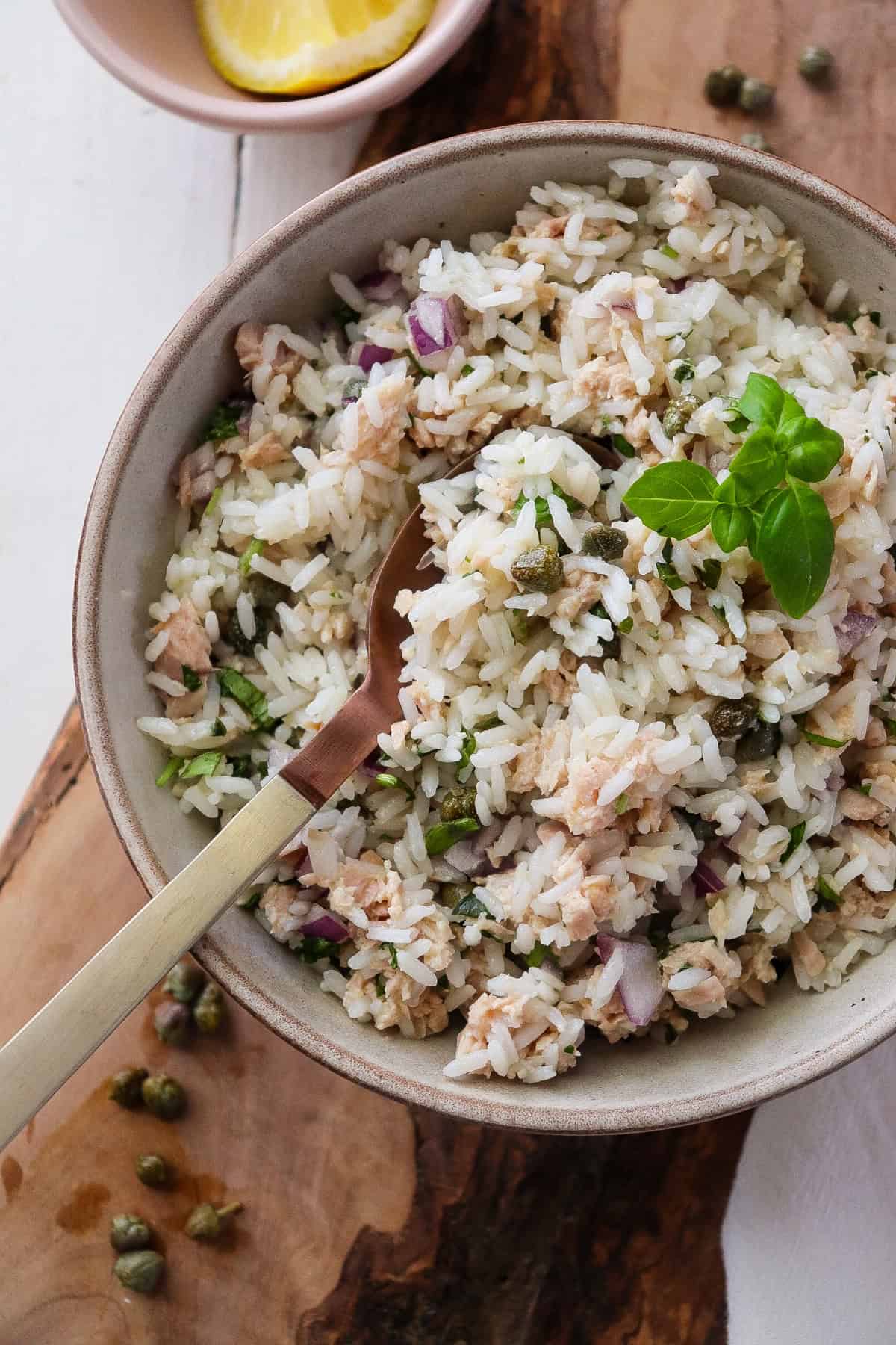 bowl of finished tuna rice salad garnished with basil with a spoon scooping a bite. 