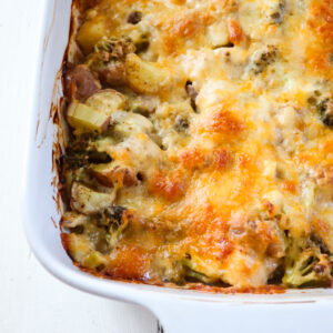 up close on finished chicken potato broccoli casserole in a white baking dish.