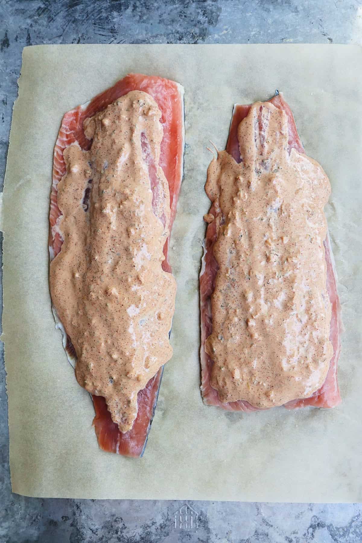two sides of salmon on a baking sheet covered in mayo mixture but uncooked.