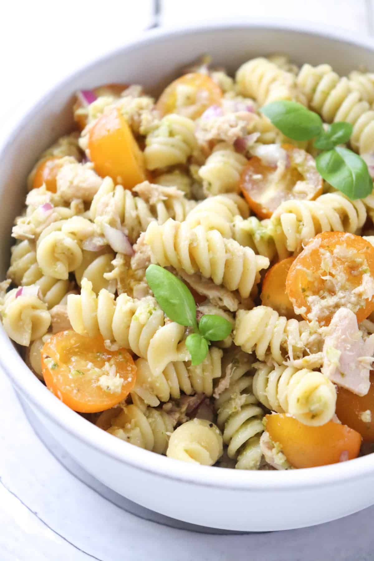 bowl of tuna pesto pasta garnished with fresh basil.