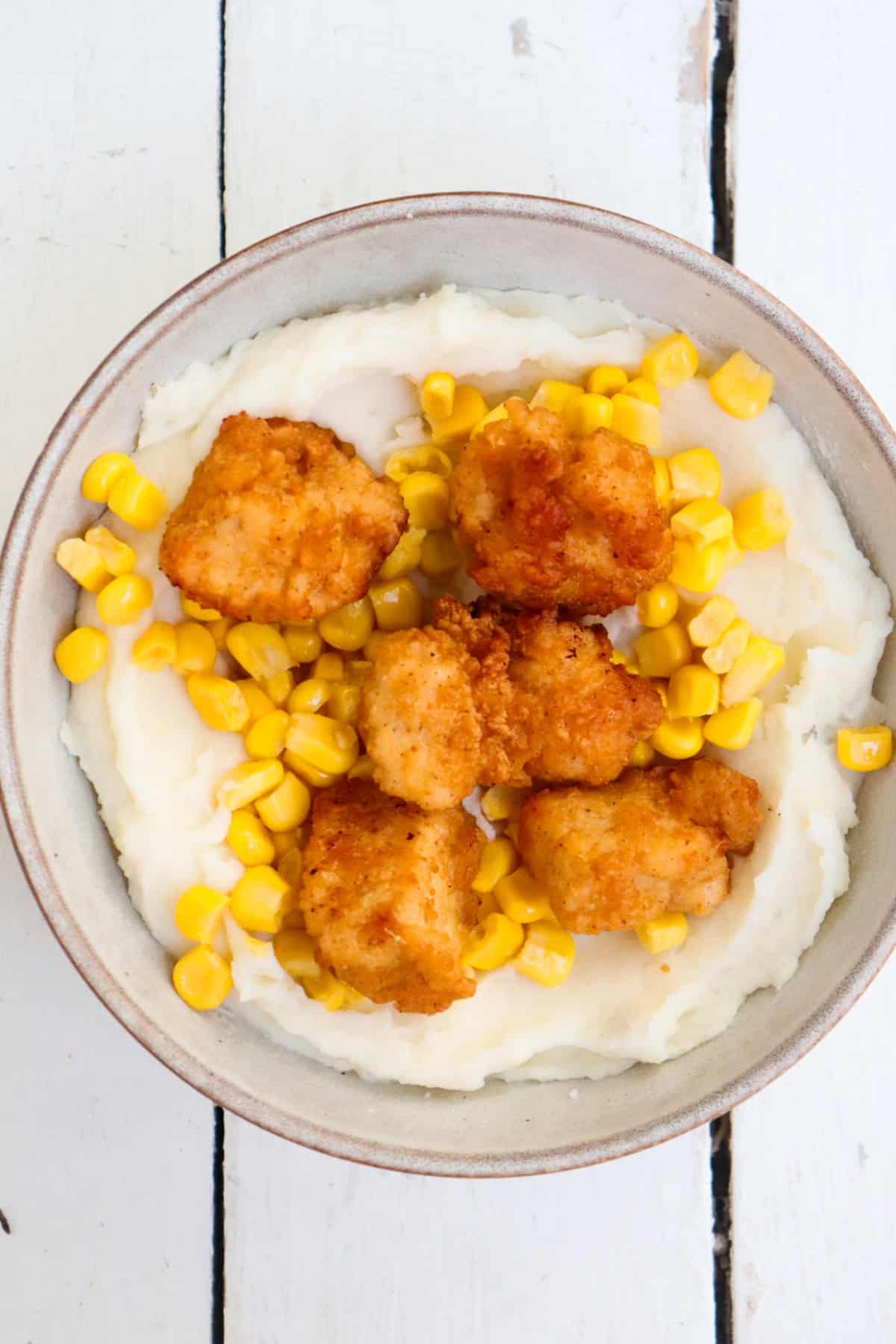 corn and popcorn chicken on top of a bed of mashed potatoes.