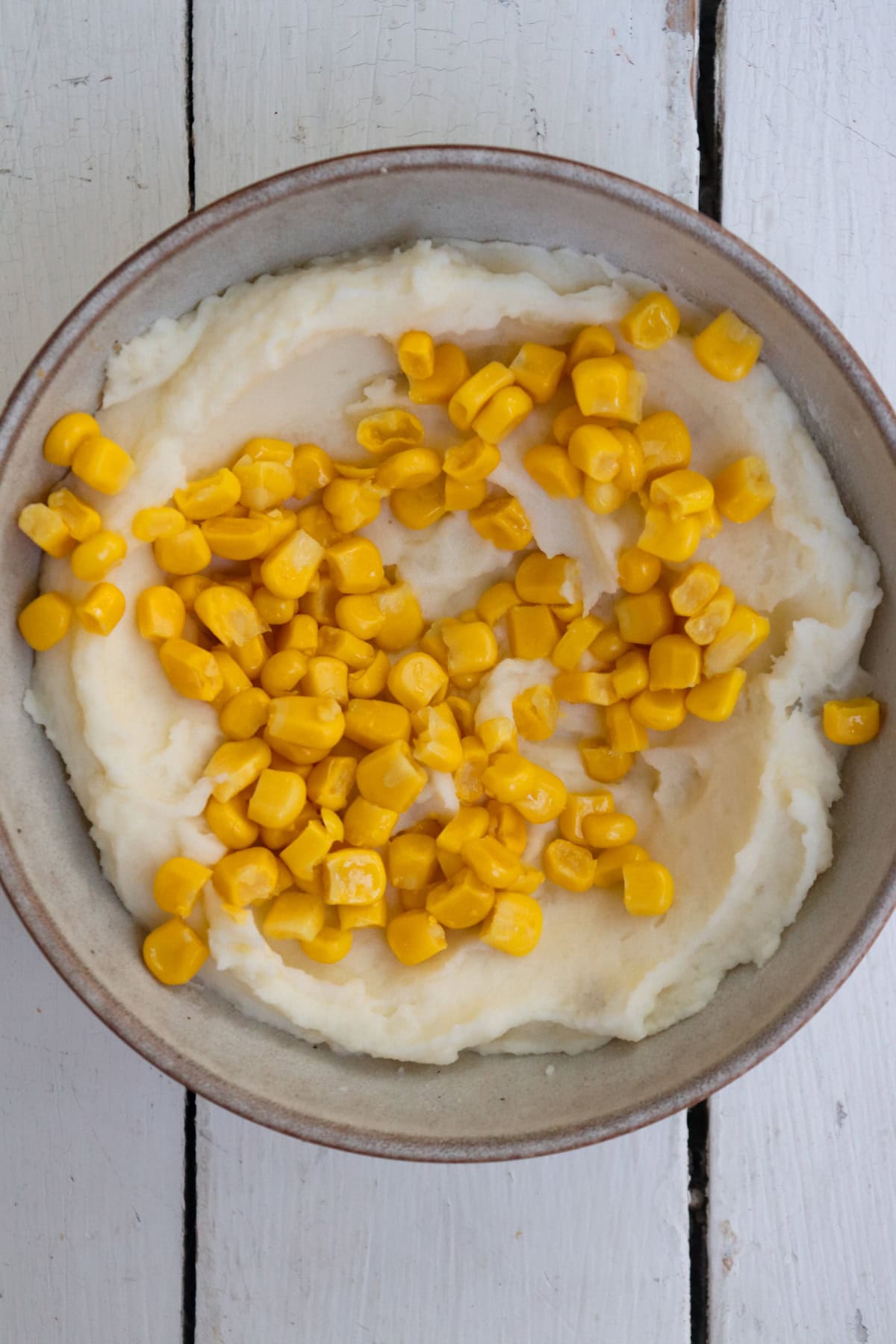 mashed potatoes in a bowl topped with corn kernels.