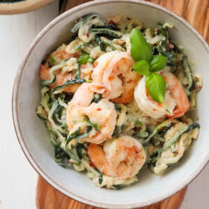 finished shrimp and zoodles in a grey bowl, topped with fresh basil.