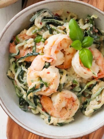 finished shrimp and zoodles in a grey bowl, topped with fresh basil.