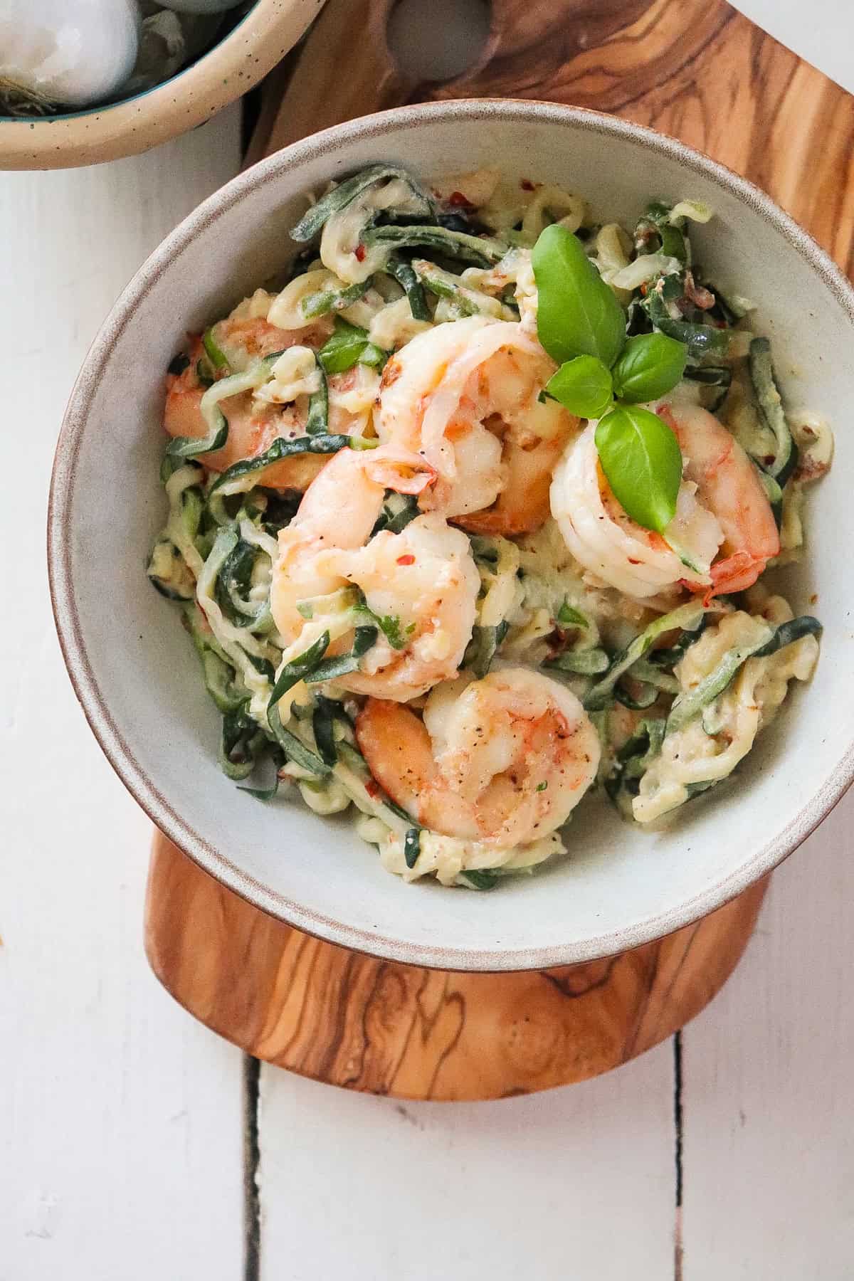 finished shrimp and zoodles in a grey bowl, topped with fresh basil.