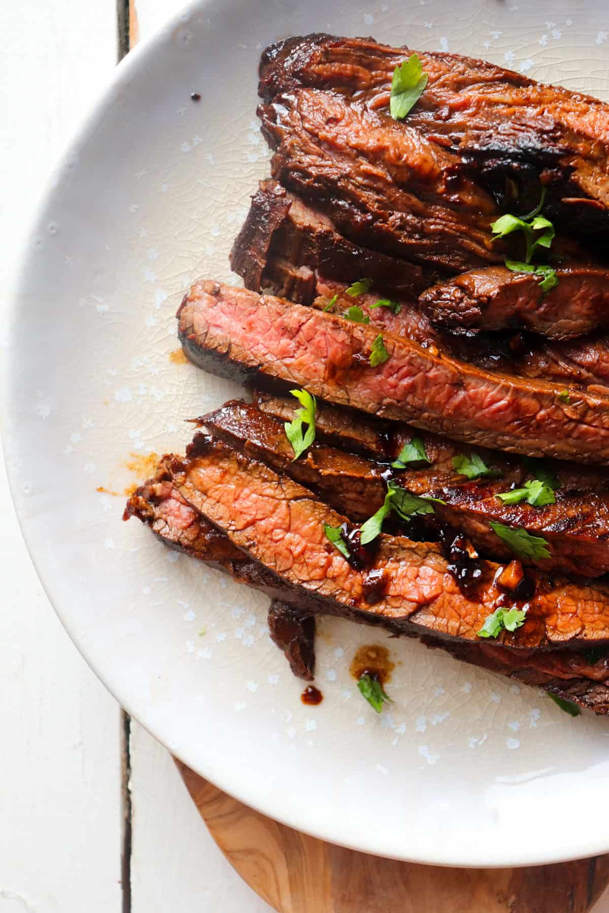 cast iron flank steak sliced and placed on a white plate with a parsley garnish.