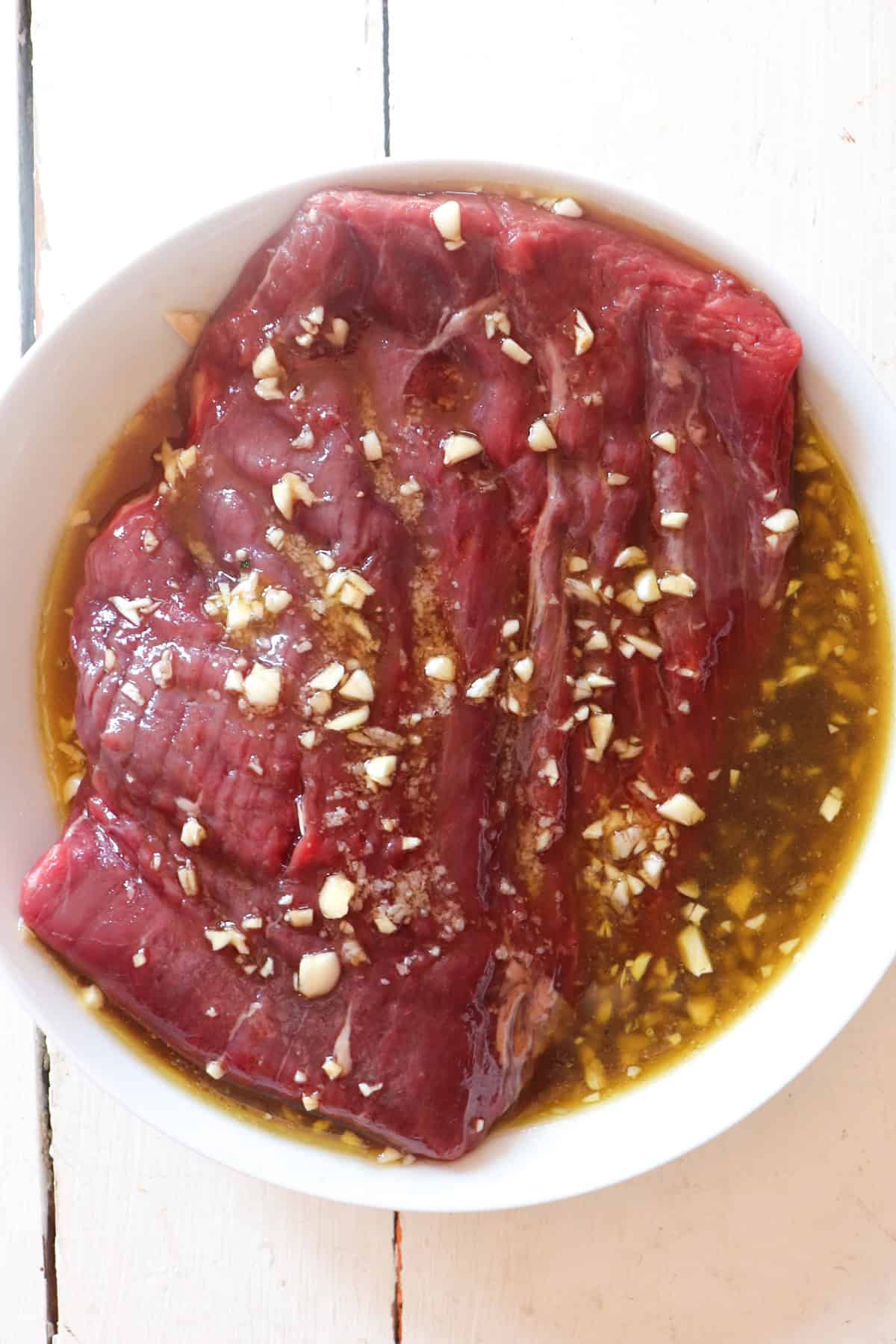 flank steak soaking in a bowl of marinade.