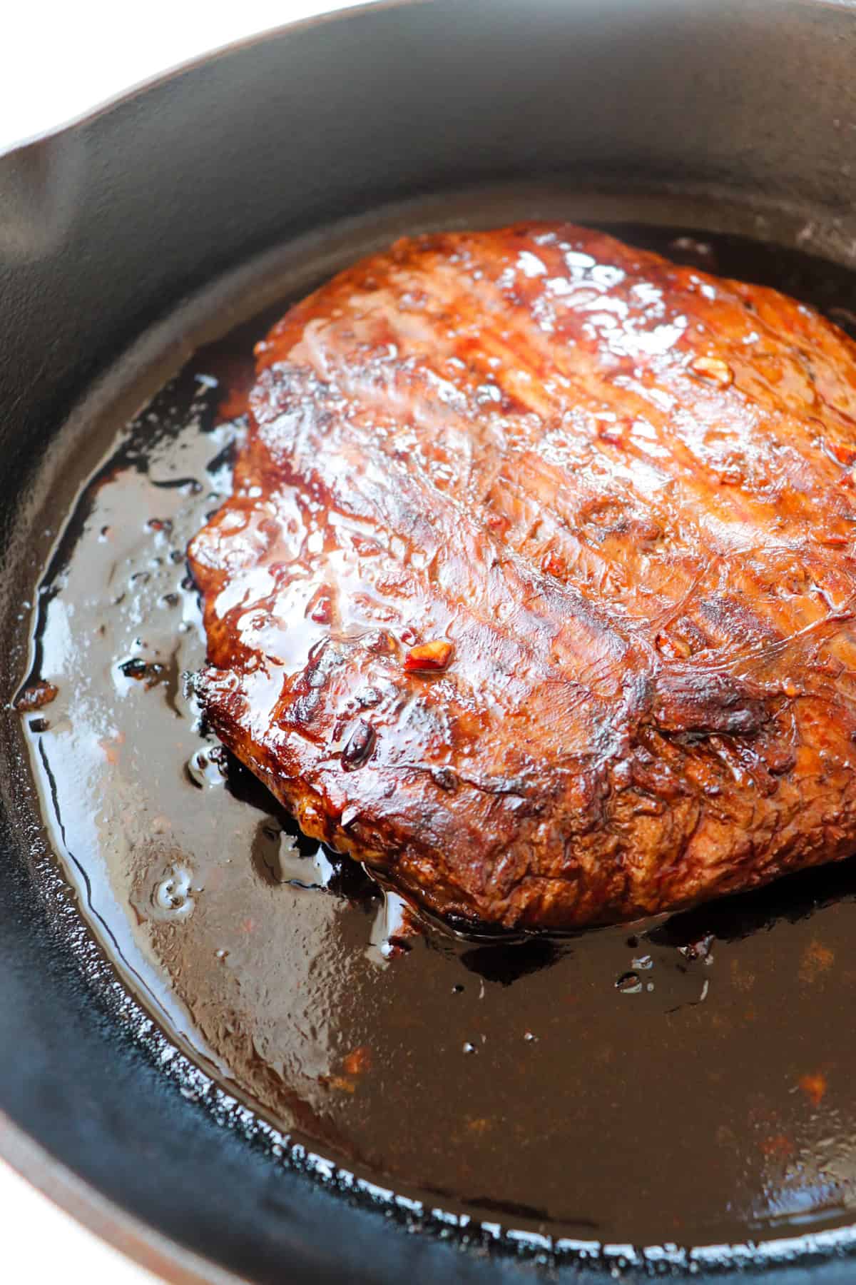 flank steak cooking on a cast iron skillet.