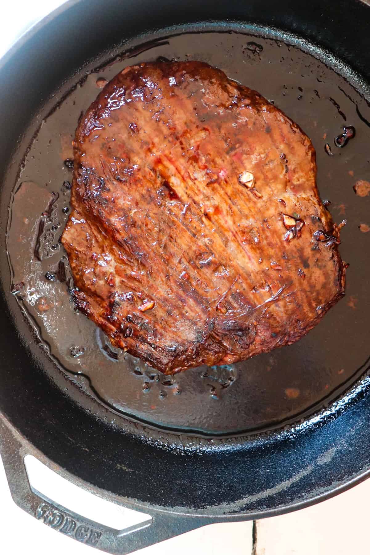 flank steak cooking on a cast iron skillet.