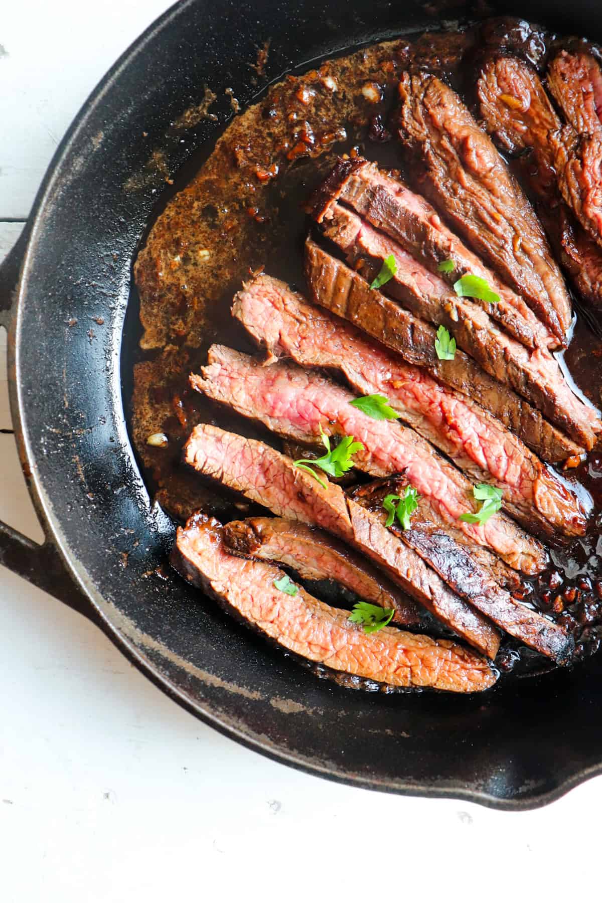 sliced flank steak resting on a cast iron skillet.