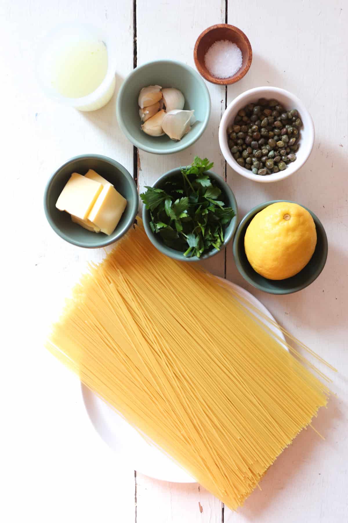 ingredients for pasta with lemon and capers on a white table.