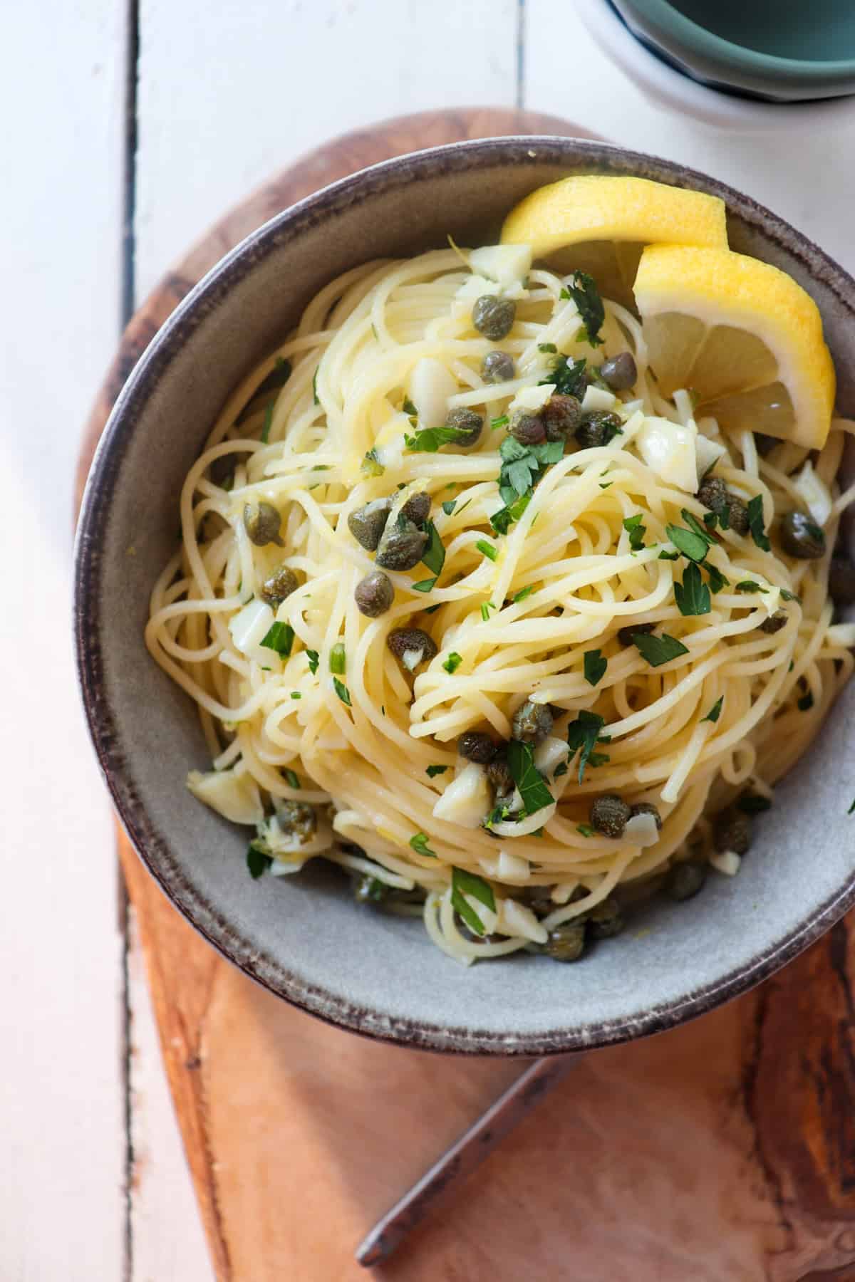 bowl of lemon caper pasta garnished with fresh lemons.