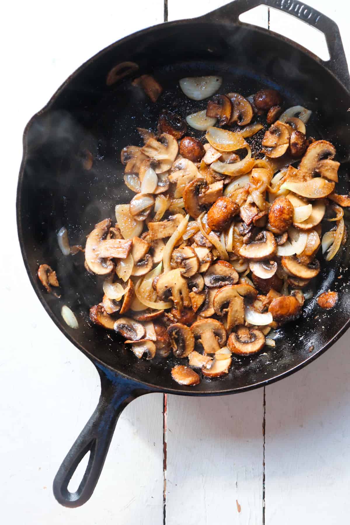 seasonings added to mushrooms and onions in a cast iron skillet.