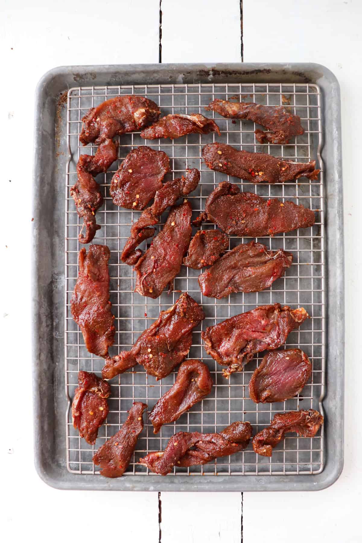 marinated venison slices on sheet pan.