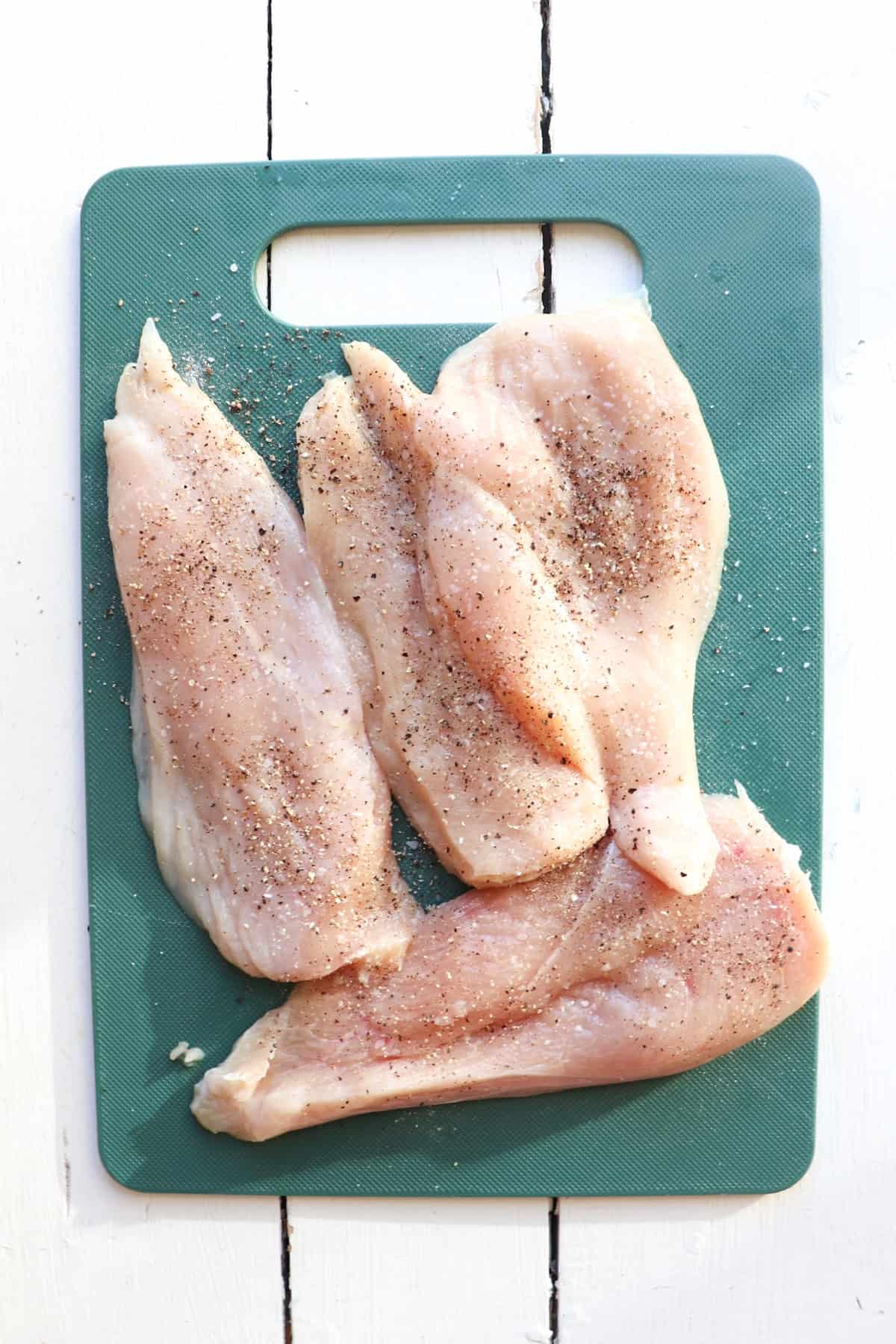 raw thin cut chicken breasts on cutting board.