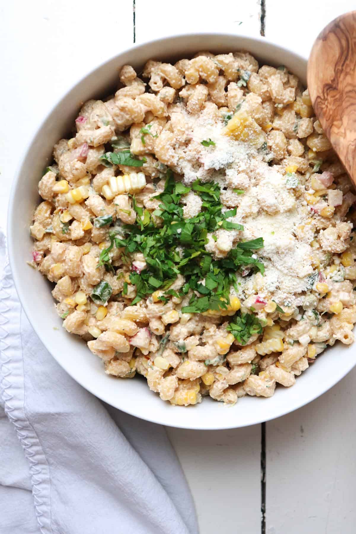 elote pasta salad with seasoning and cheese on top in mixing bowl. 