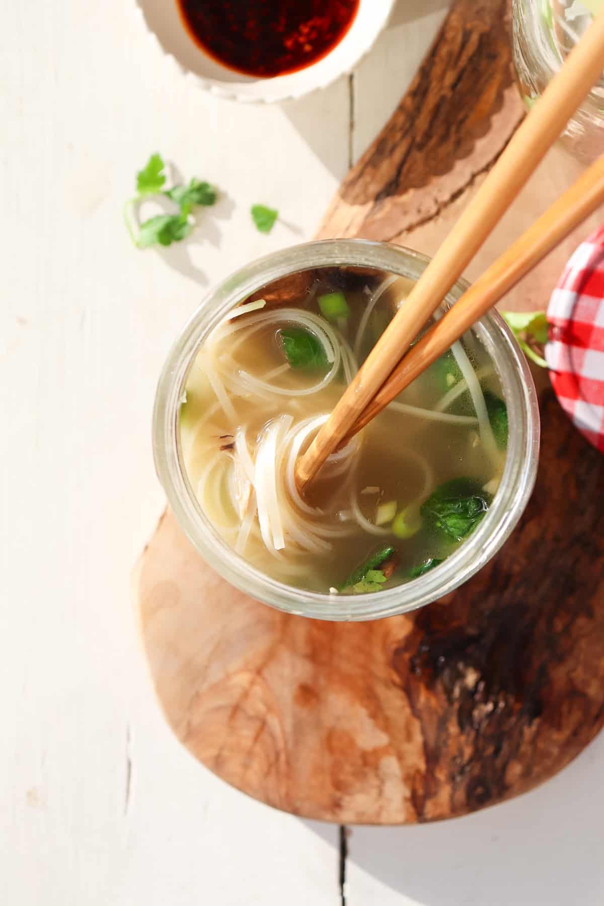 chop sticks twisting noodles in mason jar noodle cup.