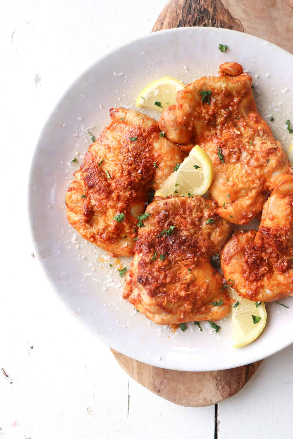 platter of garlic parmesan chicken thighs garnished with lemon and parsley.